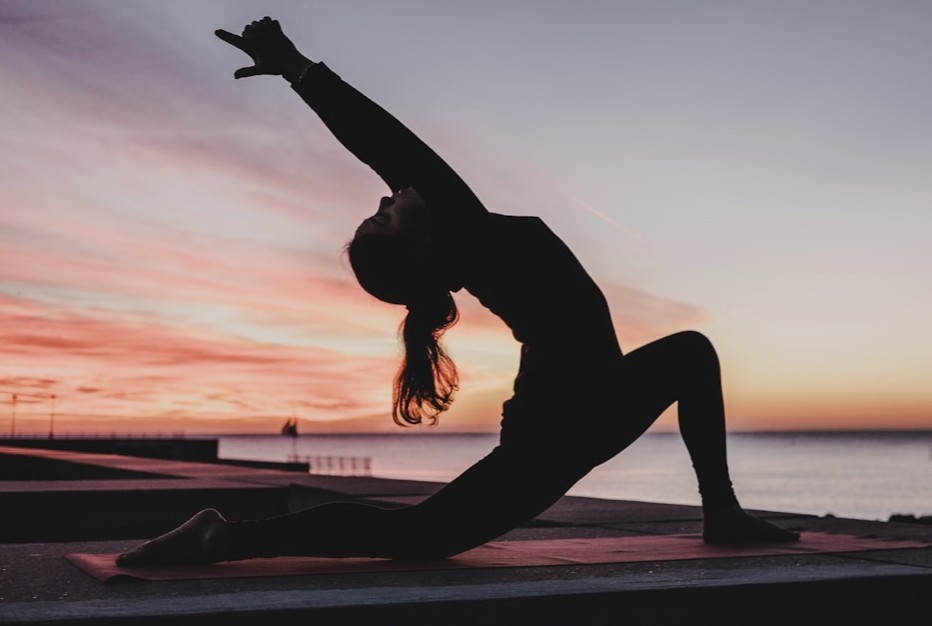 Silhouette of a person doing yoga on a mat on a pier beside the ocean at sunrise